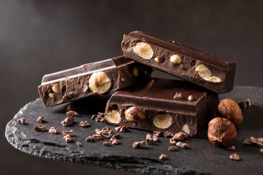 Broken pieces of dark chocolate with hazelnuts on a slate slab with cocoa nibs scattered around