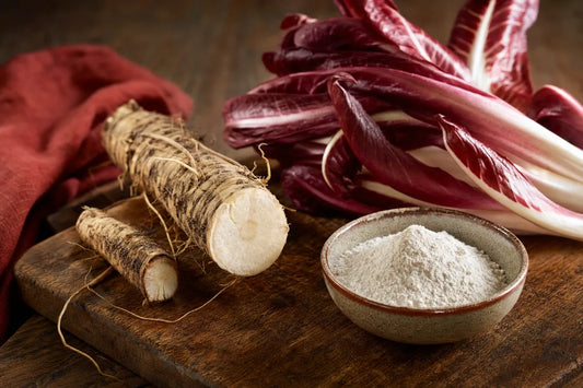 Fresh chicory root and leaves next to a small bowl of fine white powder on a wooden board