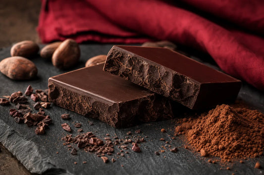 Broken slab of dark chocolate on slate with cocoa beans, nibs and cocoa powder