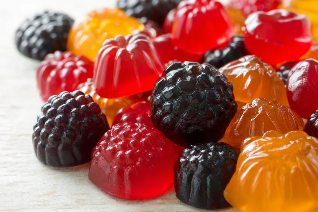 A close view of glossy fruit jelly sweets in red, amber and deep purple heaped on a pale birch table