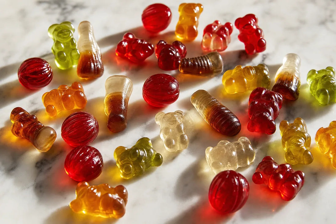 Unwrapped gummy bears, cola bottle gummies and boiled sweets scattered on white marble