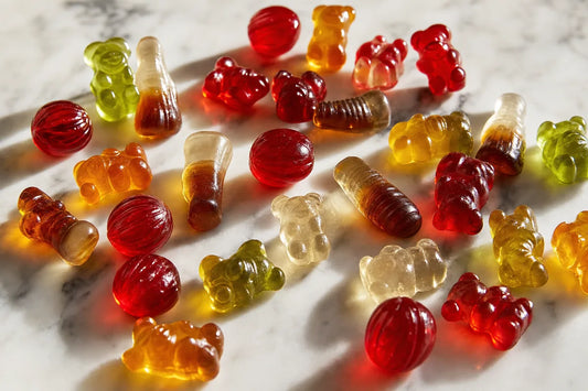 Unwrapped gummy bears, cola bottle gummies and boiled sweets scattered on white marble