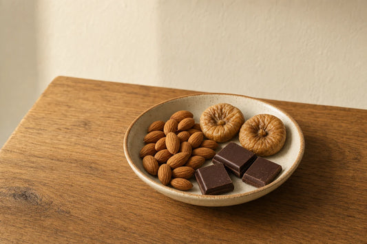 A dish of almonds, two dried figs and three squares of dark chocolate on an oak table
