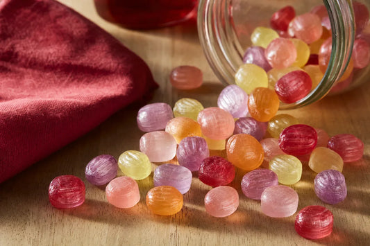 Pastel coloured boiled sweets spilling from a glass jar onto a wooden table