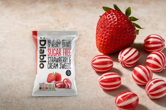 Diablo Sugar Free Strawberry and Cream Sweets 75 g bag on a pale stone worktop beside unwrapped striped sweets and a fresh strawberry