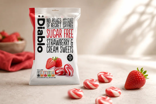 Diablo sugar free strawberry and cream sweets bag beside unwrapped red and white sweets and a fresh strawberry