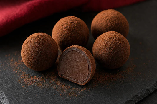 Dark chocolate truffles dusted with cocoa on slate, one cut in half to show a smooth ganache centre
