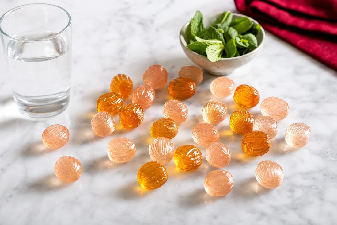 Amber and pale rose boiled sweets scattered on a marble counter beside a glass of water and a bowl of mint leaves