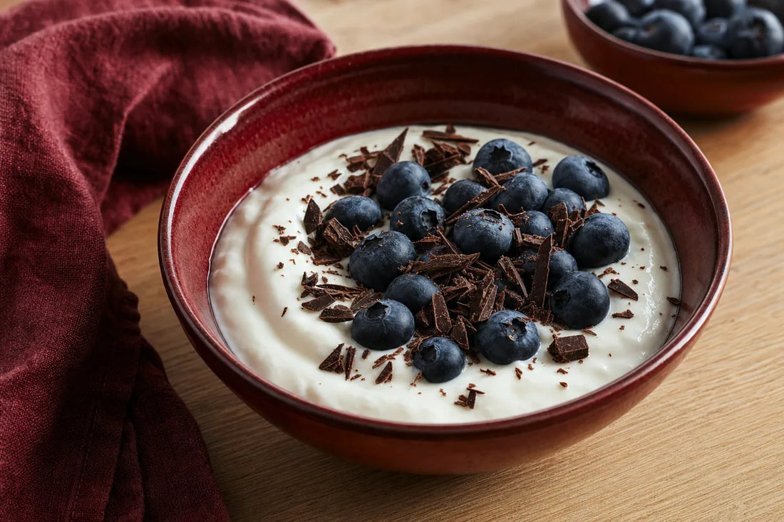 A bowl of plain yoghurt topped with blueberries and shaved dark chocolate